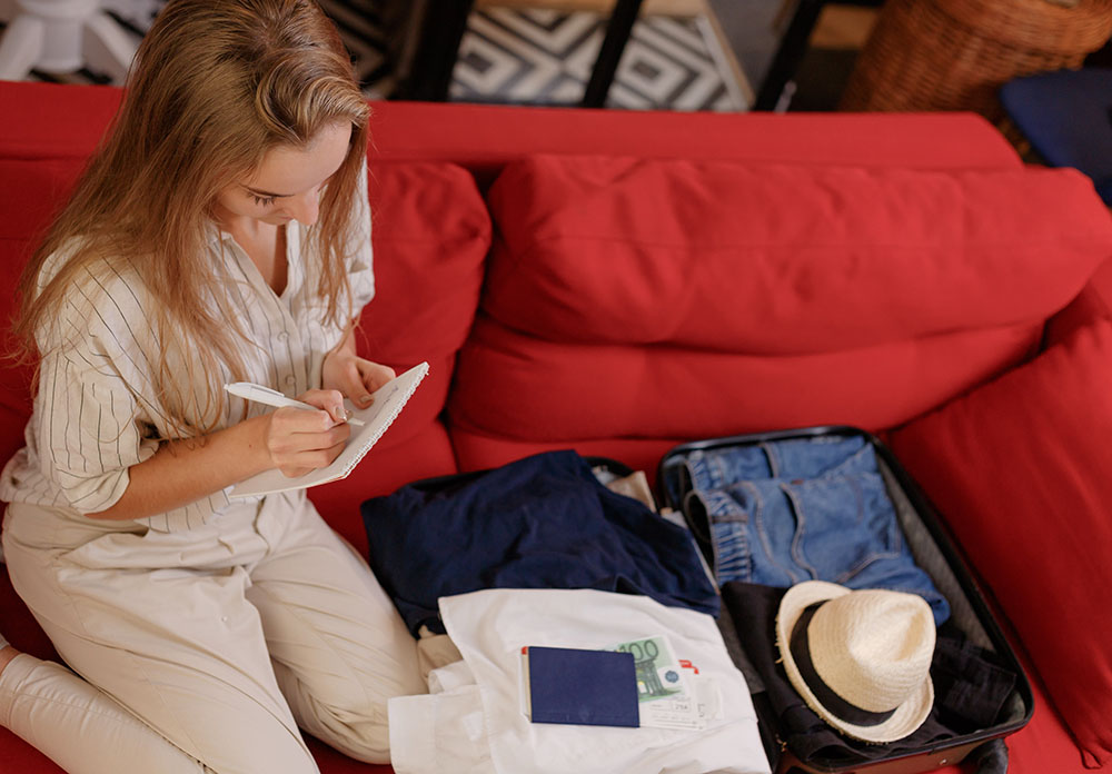 Junge Frau, die zu Hause auf der Couch Accessoires und Sachen im Gepäck überprüft
