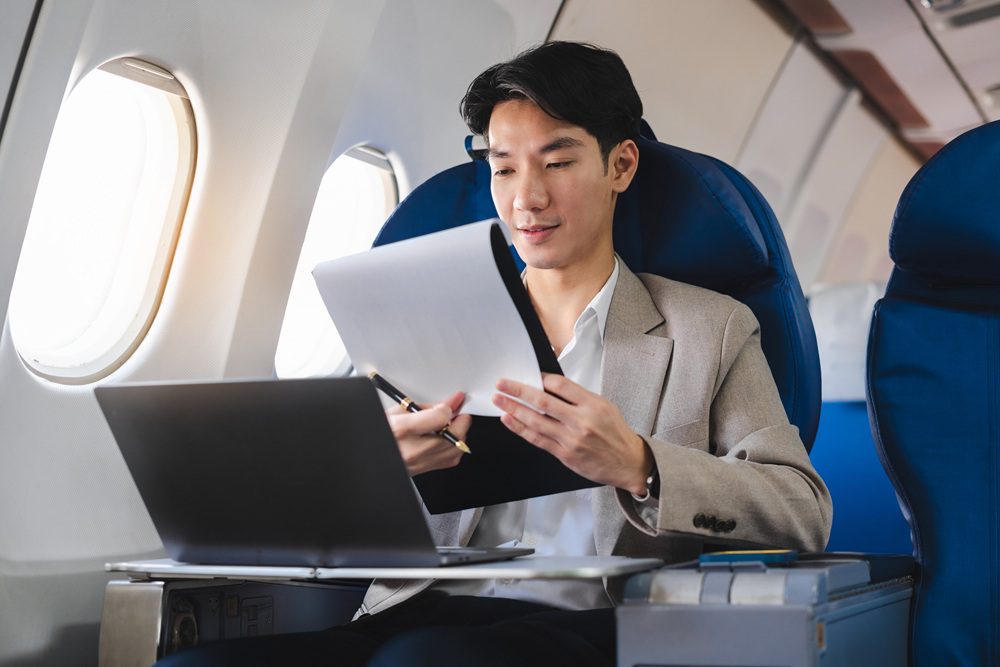 Man working from the plane on laptop with paper in hands