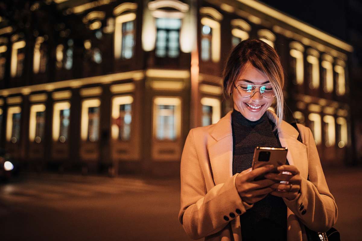 Woman looking at mobile in front of lit-up building at night