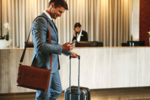 Businessman in hotel lobby with cell phone and suitcase