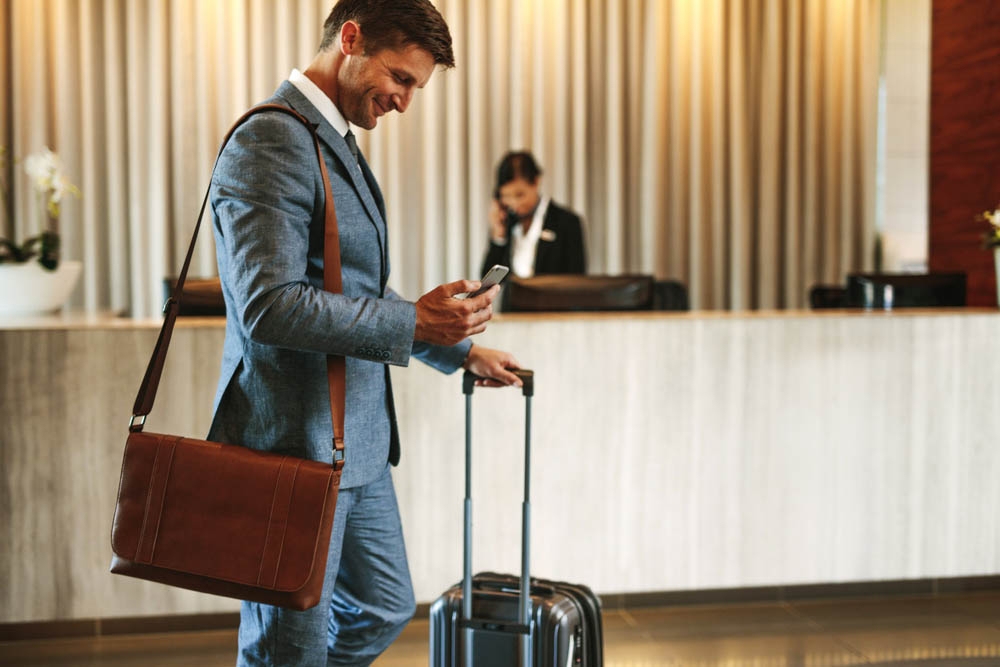 Businessman in hotel lobby with cell phone and suitcase
