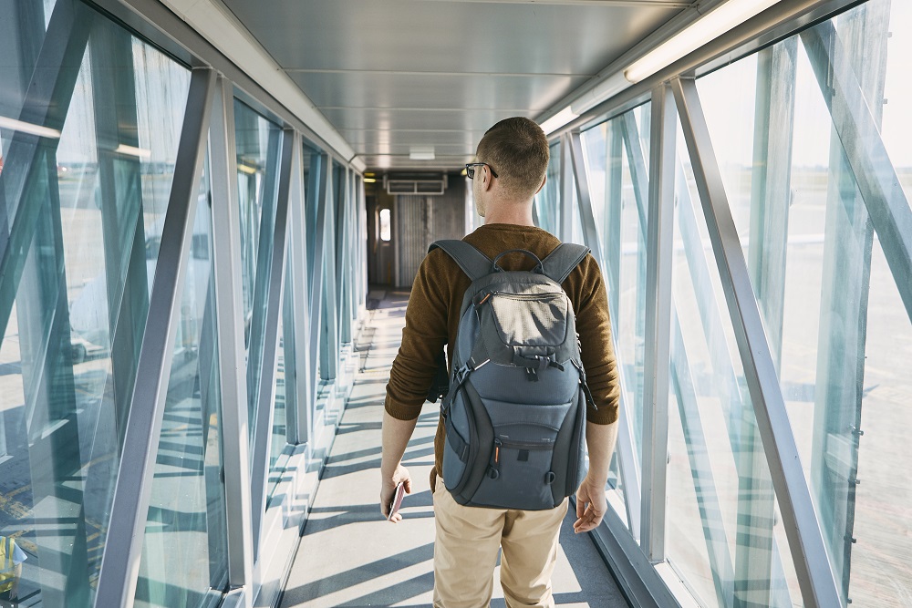Business traveler walking down jet bridge to airplane with backpack