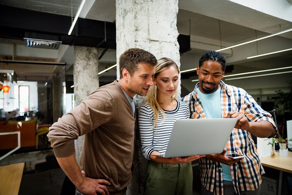 Three colleagues from remote teams collaborating in the office looking at a computer screen