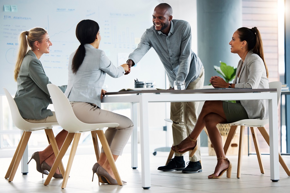 Diverse group meeting in an office setting with man standing up and shaking hands