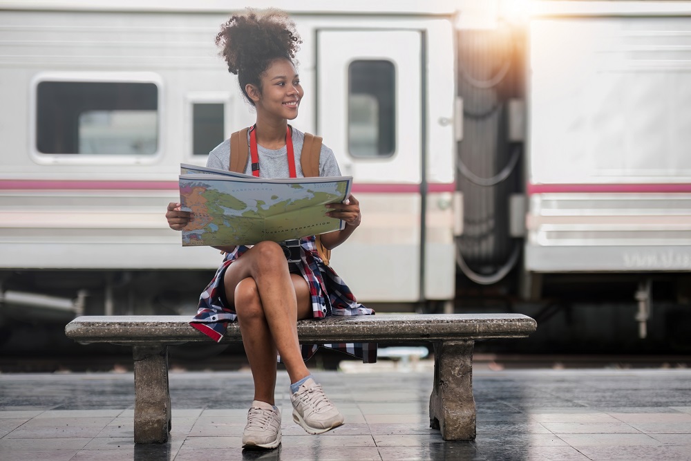 woman sitting on a bench at the train station holding a map on a bleisure trip