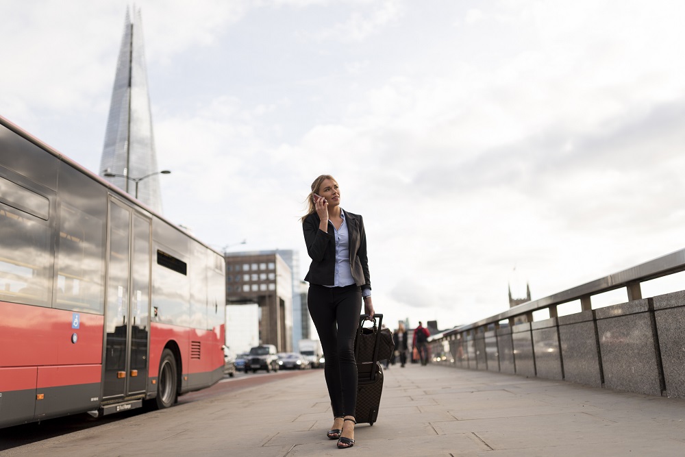 Businesswoman walking with luggage on the phone in London
