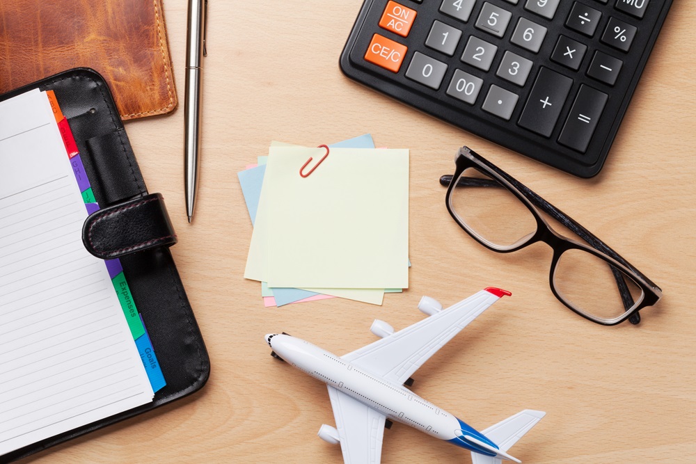 Calculating travel costs with calculator, airplane, glasses and agenda on the desk