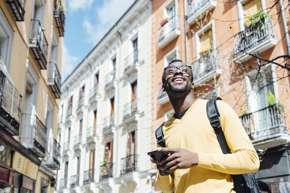 Business traveler with mobile in hand and backpack on walking through streets of Madrid