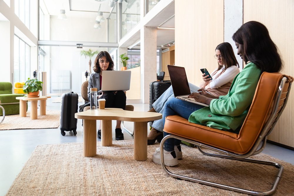 Multiracial women work using laptop in hotel lobby reception. Women working from airport lounge on their laptop