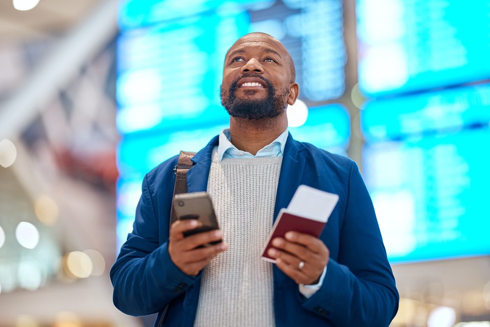 Business traveler in the airport with cell phone and airplane ticket in hand