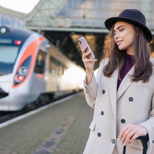 Stylish girl stands at the railway station with smartphone in  hands and waiting for the train