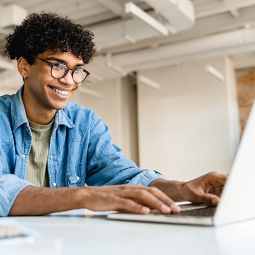 Man with glasses smiling while using laptop